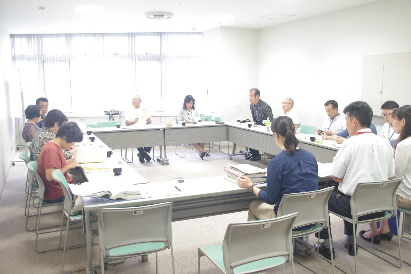 ロの字型に並べられた長机を14人ほどで囲み、東海村地域福祉計画推進会議をしている画像