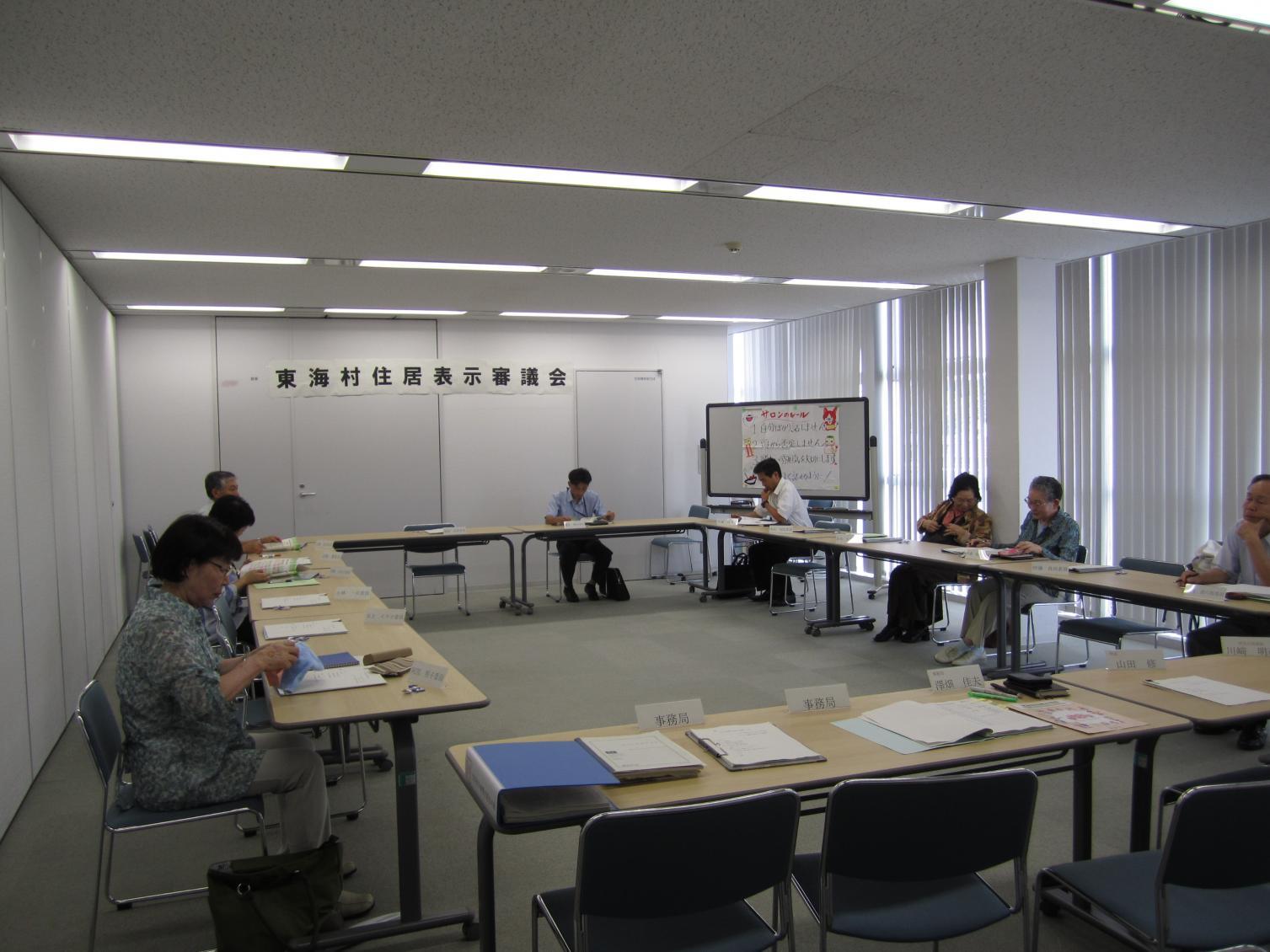 東海村住居表示審議会において、会議室にロの字型に並べられた机に向かって会議を進める参加者、8名ほどが写っている写真