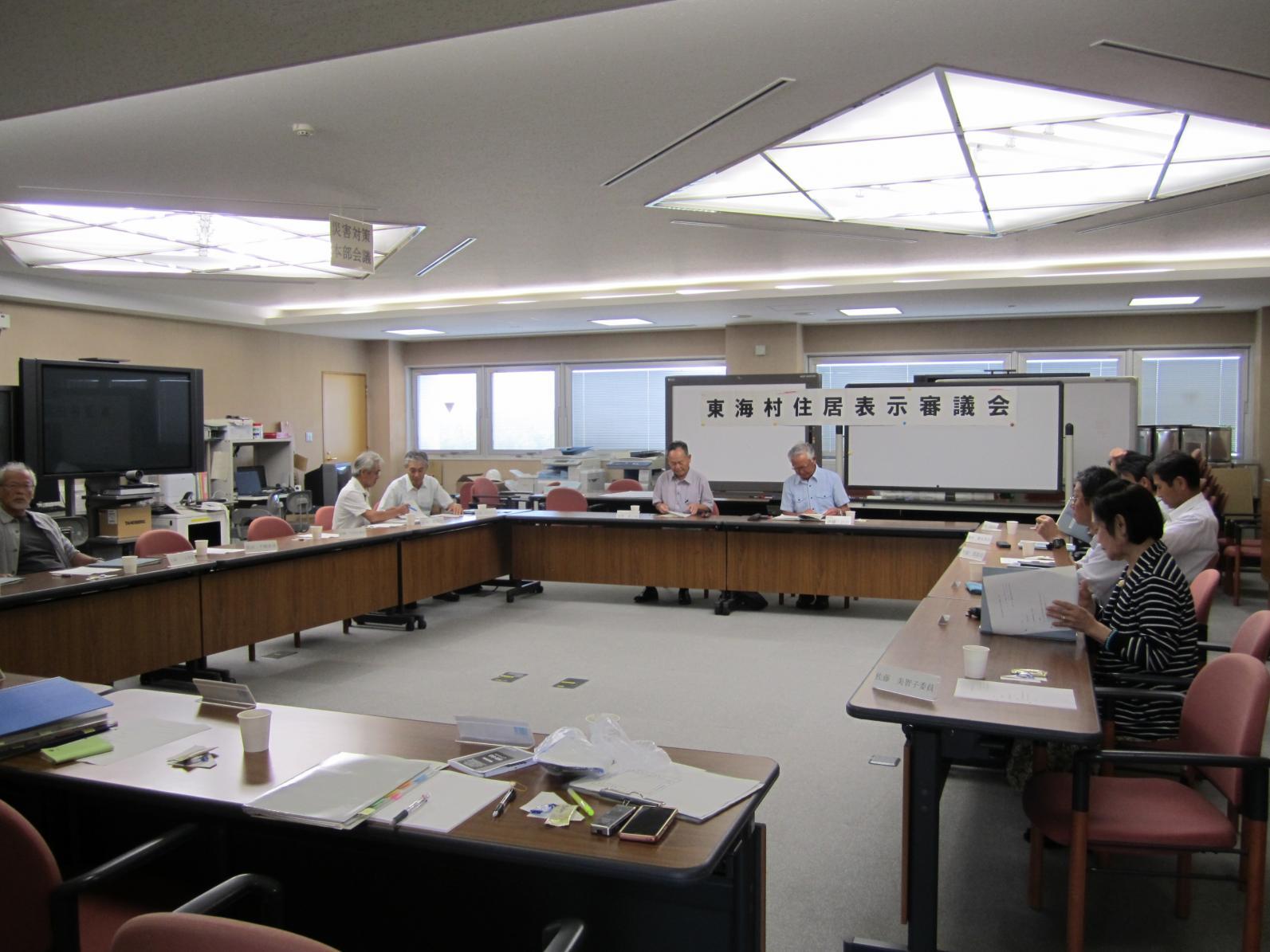 東海村住居表示審議会において、会議室にロの字型に並べられた机に向かって会議を進める参加者、9名ほどが写っている写真