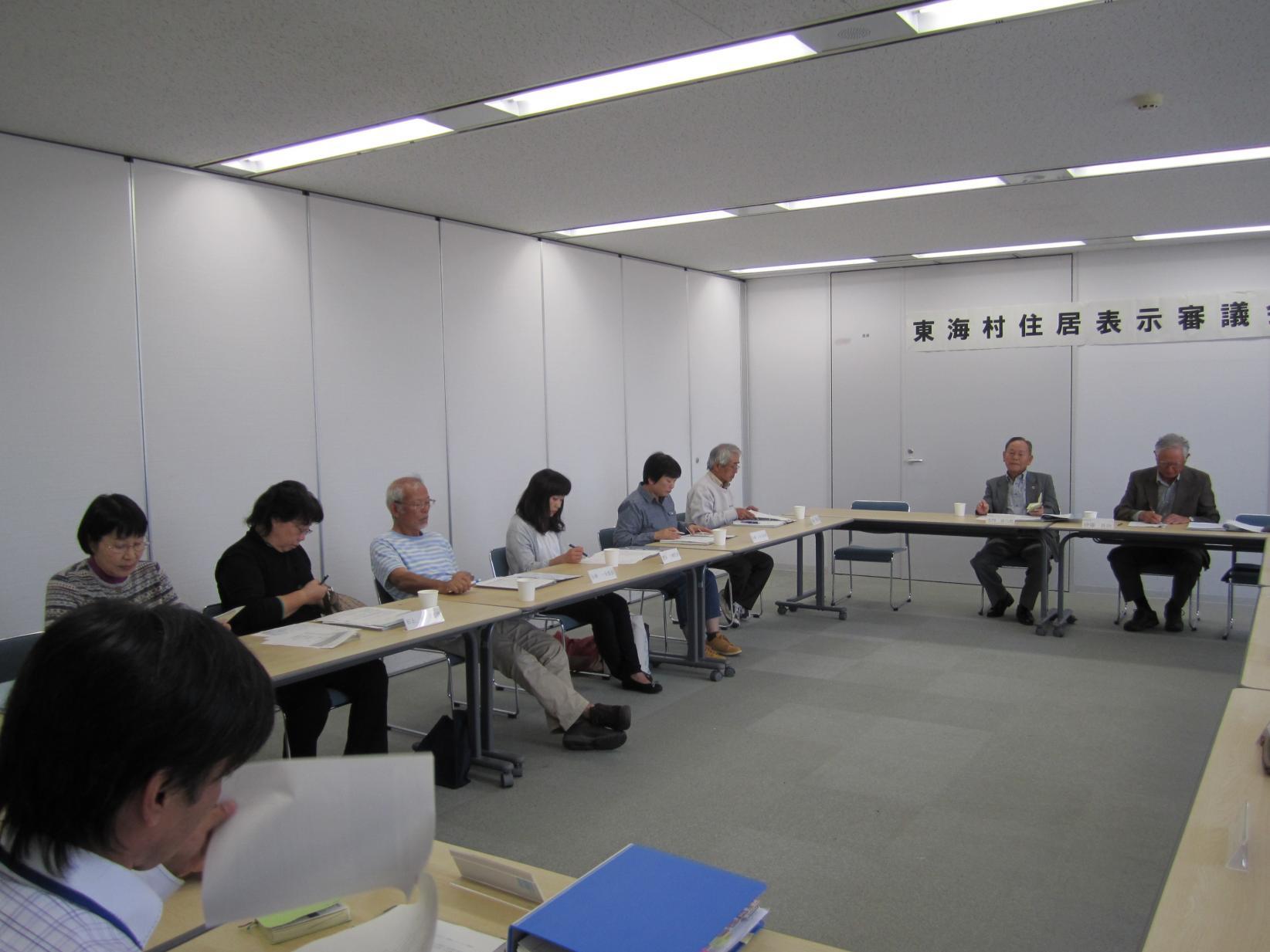 東海村住居表示審議会において、会議室にロの字型に並べられた机に向かって会議を進める参加者、9名ほどが写っている写真