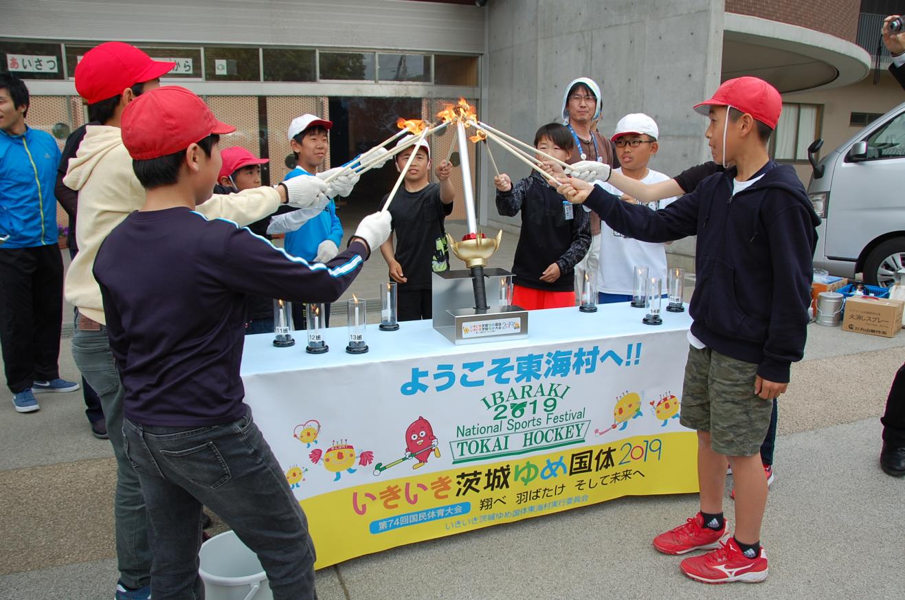 トーチの先を合わせて火をともしている赤白帽をかぶった小学生たちの写真