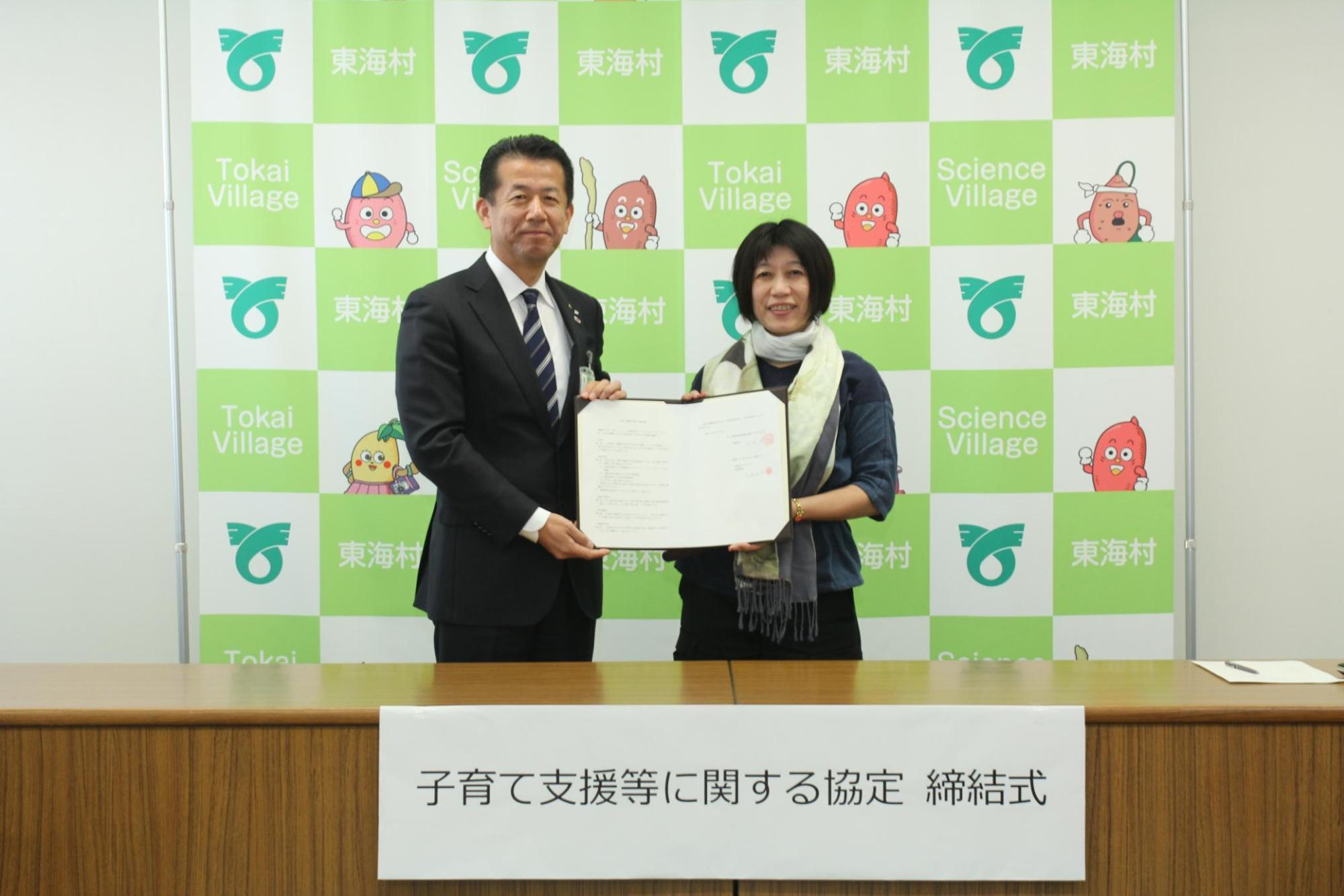 東海村村長と有限会社モーハウスの代表が2人で協定書を掲げている写真