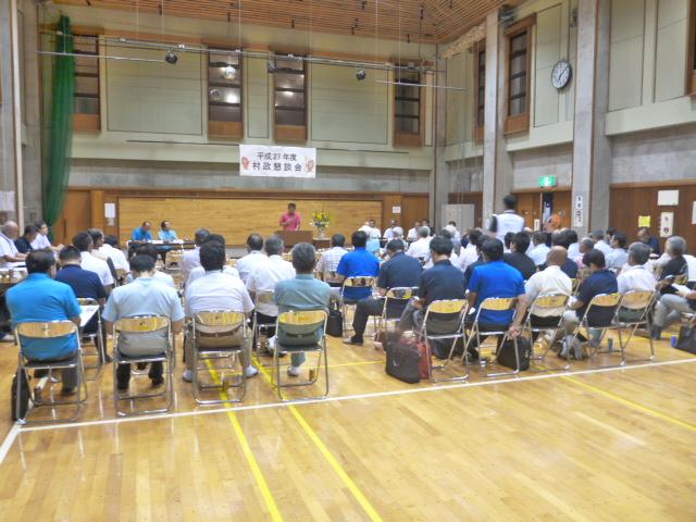 村松地区村政懇談会で、前に立ちマイクを持って話す男性とホールに並んだ椅子に座り話を聞いている参加者たちの写真