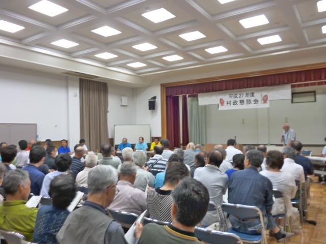 舟石川・船場地区村政懇談会で、前に立ちマイクを持って話す男性とホールに並んだ椅子に座り話を聞いている参加者たちの写真