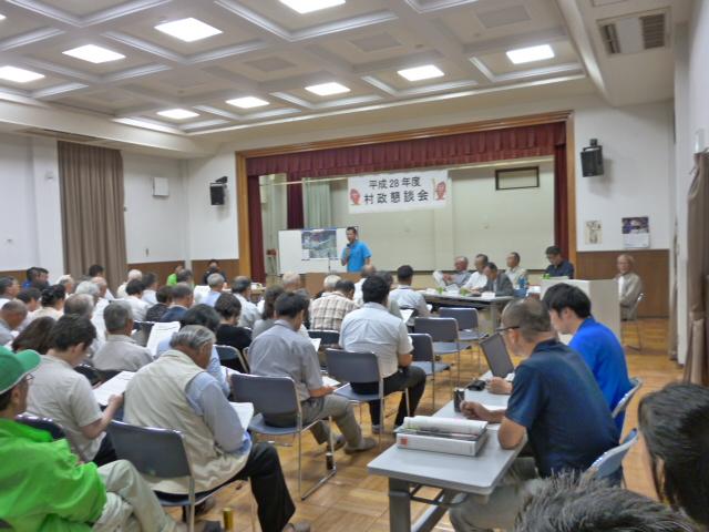 舟石川・船場地区村政懇談会にて、前に立って話をしている男性と資料を見ながら話を聞いている参加者たちの写真