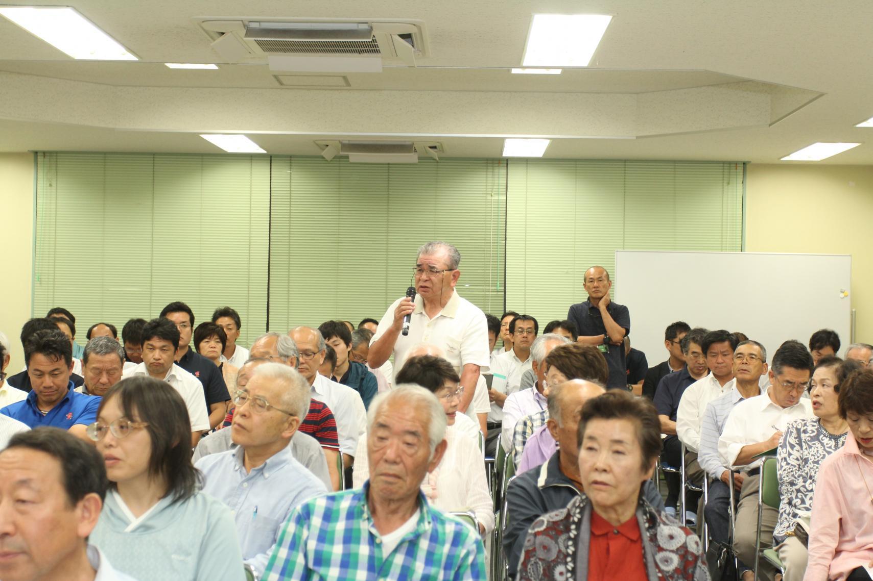 真崎地区村政懇談会にて、客席側でマイクを持ち席を立って意見を述べている男性と意見を聞いている参加者たちの写真