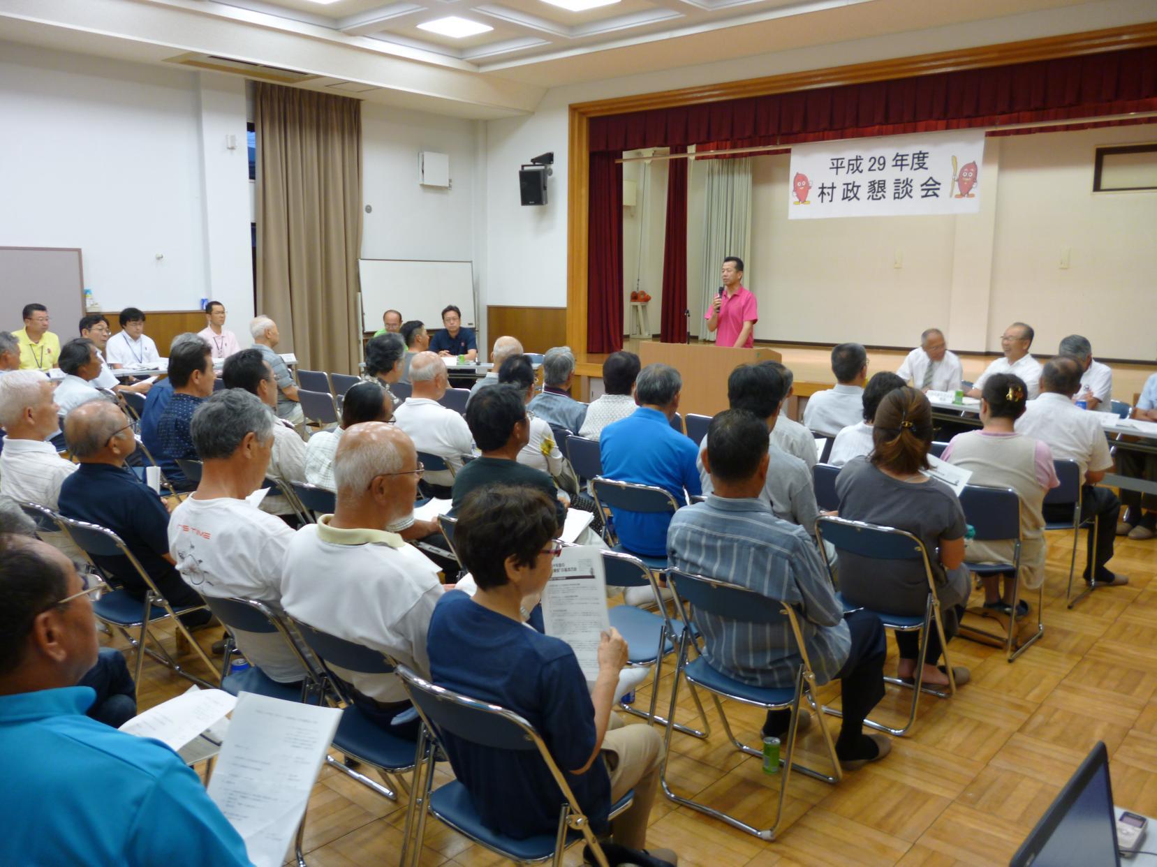 舟石川・船場地区村政懇談会にて、前に立ちマイクを持って話をしている男性と席に座り話を聞いている参加者たちの写真
