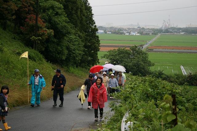 傘を差し、カッパを着た人たちが坂道を歩いている写真