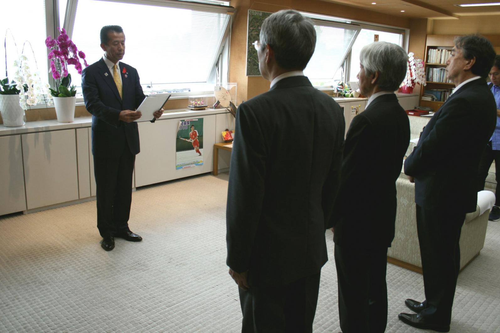 要請文を読み上げる山田村長と後姿の男性3人の写真