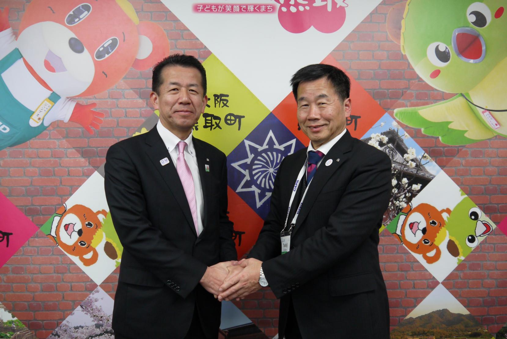 藤原町長と山田村長が笑顔で握手している写真