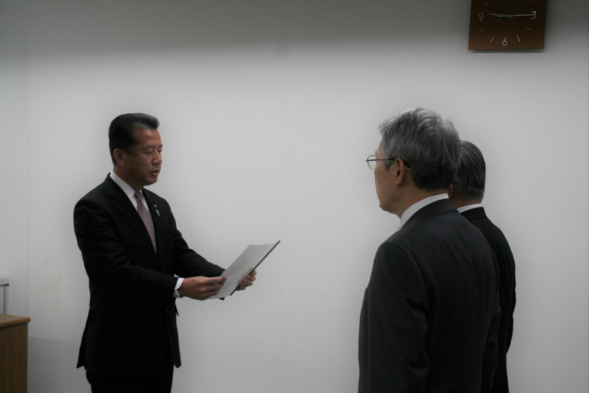 文書を読み上げる村長と向かい合う位置に立って聞いている山本理事、三浦所長の写真